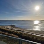 Blick auf Strand und Meer bei Sonnenaufgang mit Holzbank und Dünen.