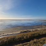 Weitläufiger Strand mit Wattgebieten und trockenem Uferbereich unter blauem Himmel.