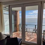 Durch Glastüren führt ein Balkon mit Tisch und Stühlen zum Meer.