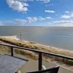 Terrasse mit Tisch und Stühlen bietet Blick auf Strand und Meer.