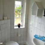 Badezimmer mit Fenster, Waschbecken und Toilette. Auf dem Fensterbrett steht eine Pflanze.