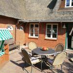 Terrasse mit Tisch, Stühlen und Strandkorb vor einem Haus mit Strohdach.