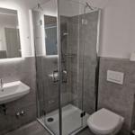 Badezimmer mit Dusche, Waschbecken und Toilette. Fliesen und Spiegel sind modern.