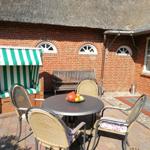 Terrasse mit Tisch, Stühlen und Strandkorb vor Backsteinhaus mit Dach