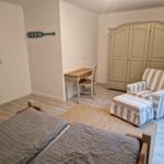 Zimmer mit Doppelbett, Schreibtisch, Sessel und Kleiderschrank.