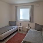 Zwei Einzelbetten mit grauer Bettwäsche, zwei Nachttische und ein Fenster mit Vorhängen.