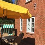 Roter Backsteinbau mit Terrasse, gelber Sonnenschirm und grün-weißem Liegestuhl.