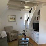 Wohnzimmer mit Sofa, Sessel, Fernseher und Treppe.