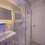 Badezimmer mit Dusche, Waschbecken und beleuchtetem Spiegel