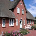 Rotes Backsteingebäude mit Strohdach, weißer Tür und Blumenbeete.