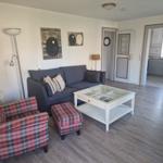 Wohnzimmer mit Sofa, Sessel und Glas-Tisch. Küche und Flur sind sichtbar.