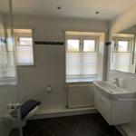 Badezimmer mit Dusche, Waschbecken und Toilette. Fenster mit Jalousien.