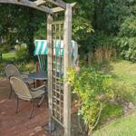 Gartenbereich mit Holzarkade, Tisch, Stühlen und grün-weißem Sonnenschirm.