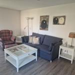 Wohnzimmer mit Sofa, Sessel, Tisch und Wandbildern.