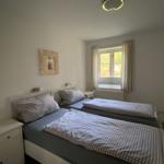 Zwei Betten mit karierten Bettwäsche, Fenster mit Vorhängen, Nachttisch und Wandbild.