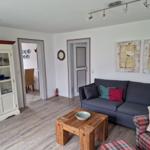 Wohnzimmer mit Sofa, Couchtisch und Schrank. An der Wand hängen zwei Blumenbilder.