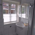 Badezimmer mit Waschbecken, Spiegelschrank und Dusche. Fenster mit Jalousie.