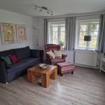 Wohnzimmer mit Sofa, Sessel und Holztisch. Fenster mit Vorhängen und Fernseher.