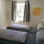 Zwei Betten mit karierten Bettwäsche, Fenster mit Streifenstoren und Wandbilder.