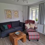 Wohnzimmer mit Sofa, Sessel und Holztisch. Fenster mit Vorhängen und Wandbildern.