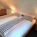Schlafzimmer mit Doppelbett, zwei Nachttischen und Lampen. Holzmöbel und schräger Dachfirst.