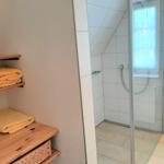 Bad mit Dusche, Holzregal und gelben Handtüchern.