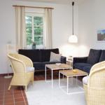 Wohnzimmer mit zwei Sofas, zwei Stühlen und einem Tisch. Fenster mit Vorhängen und Wandbilder.