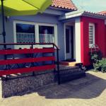 Rot-weißes Haus mit Terrasse, grüner Sonnenschirm und roter Bank.