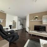Living and dining area with kitchen, TV, and black leather chair.