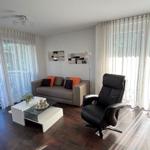 Living room with sofa, chair, and glass table near large windows.