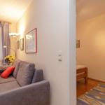 Wohnbereich mit Sofa und Schlafzimmer mit Bett und Kleiderständer