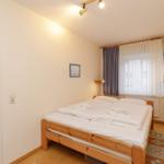 Schlafzimmer mit Holzbett, Fenster und Tür.