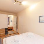Schlafzimmer mit Bett, Kleiderschrank und Spiegel. Deckenleuchte und Wandbild.