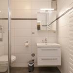 Badezimmer mit Dusche, Waschbecken und Toilette. Weiße Fliesen und Heizung.