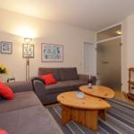 Wohnzimmer mit grauem Sofa, roten Kissen, Holztisch und Fernseher.