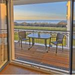 Terrasse mit Tisch und Stühlen, Blick auf Meer und Wiese.