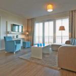 Wohnzimmer mit Sofa, Sessel und Balkon. Schlafzimmer im Hintergrund.