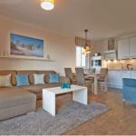 Wohnbereich mit Sofa, Couchtisch und Essbereich. Küche mit weißen Schränken.