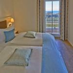 Zwei Betten mit blauen Kissen und Blick auf Balkon mit Meerblick.