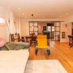 Wohnbereich mit Sofa, gelber Sessel und Klavier. Holzboden und Essbereich im Hintergrund.