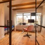 Ein Zimmer mit Schreibtisch, Stuhl und Bett hinter Glasschiebetür.