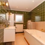 Badezimmer mit grünen Fliesen, Badewanne und Waschbecken.