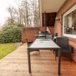 Terrasse mit Tisch, Stühlen und Grill. Holzdecke, Ziegelwand und Garten.