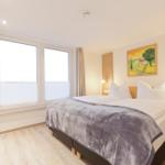 Schlafzimmer mit Doppelbett, Fenster und Wandbild.