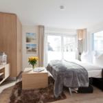 Schlafzimmer mit Bett, TV und Fensterblick auf Gebäude