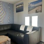 Schwarzes Ledersofa vor Wand mit 3D-Relief und Strandbildern an der Wand.