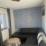 Schwarzes Sofa vor einer wellenförmigen Wand. Fenster mit Vorhängen. Tisch aus Holz.