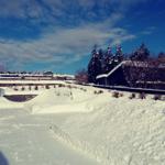 Schneebedeckter Außenbereich mit Garage und Gartenhaus unter blauem Himmel.