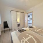 Schlafzimmer mit Bett, Kleiderschrank und Blick in die Küche.