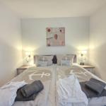 Zimmer mit zwei Betten, Seemotiv-Bettwäsche und Wandbild mit Muscheln.